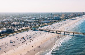 A beach with a pier extending into the ocean, surrounded by buildings and a clear sky. - The Ultimate Jacksonville Beach Getaway (Jacksonville Beach)