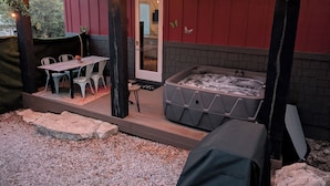 Un espacio de patio cubierto con un jacuzzi, asientos exteriores y luces colgantes.