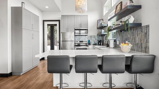 Una cocina moderna con una isla central, taburetes de bar, electrodomésticos de acero inoxidable y estantes decorativos.