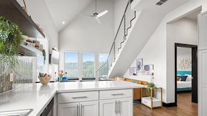 Una cocina moderna con armarios blancos, una isla grande y una escalera que lleva a un dormitorio tipo loft.