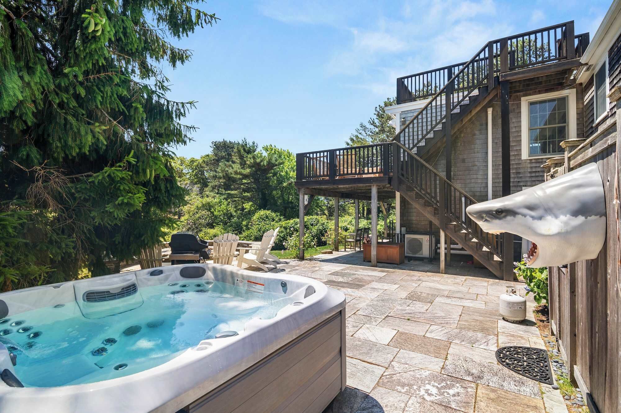 A hot tub in a backyard with a wooden deck and stairs leading to a house.