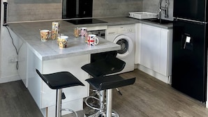 Una cocina moderna con armarios blancos, un refrigerador negro, una lavadora y dos taburetes negros.