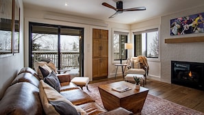 A spacious living room with a leather sofa, a coffee table, and a fireplace. There is a ceiling fan and a large window providing a view of the outdoors. - Classy, contemporary, cozy, Sun Valley condo with Resort Amenities (Sun Valley)