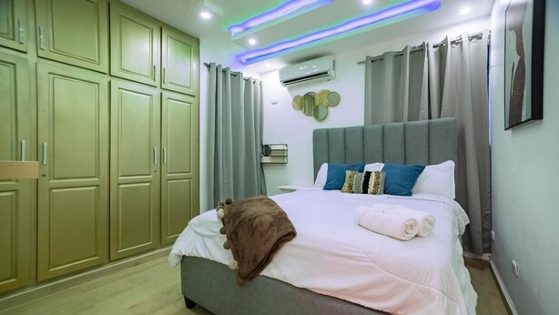 Un dormitorio con cama, cortinas, equipo de aire acondicionado e iluminación LED en el techo.