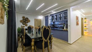 Un comedor moderno con una mesa de vidrio y sillas doradas, una cocina con armarios azules y un pasillo con diseño geométrico en la pared.