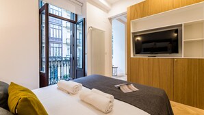 Una habitación de hotel moderna con una cama, un televisor montado en la pared y vistas de la ciudad a través de un gran ventanal.