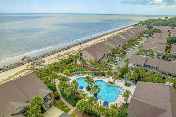 A resort with a swimming pool surrounded by palm trees, a beach, and ocean views.