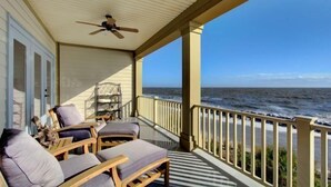 A covered porch with wooden furniture and a ceiling fan, overlooking the ocean. - Ocean Cottage 118 The Cottages at Jekyll Island Oceanfront (Jekyll Island)