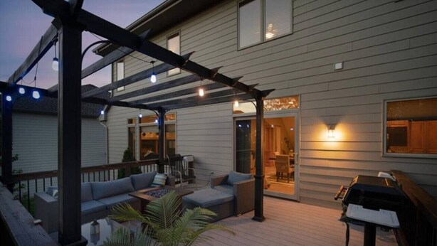 Un patio cubierto con mobiliario exterior, una parrilla y luces colgantes.