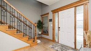 Una escalera con escalones de madera y barandillas negras, una puerta blanca con un panel de vidrio esmerilado y una pequeña planta en maceta sobre una mesita.
