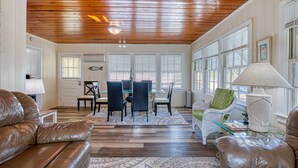 Un salón espacioso con techo de madera, un comedor con mesa y sillas de cristal, y una zona de estar acogedora con sofás de cuero y una alfombra estampada.