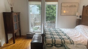 A bedroom with a bed, a wooden bench, a cabinet, and a window with a view of a backyard.