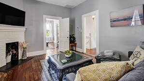 A living room with a fireplace, a glass coffee table, a sofa, and a painting on the wall.