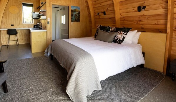 Cozy retreat with a sloped ceiling, featuring a made bed, compact kitchenette, and a desk with chair.