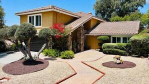 A yellow house with a tiled roof, surrounded by well-maintained landscaping and a small pond.