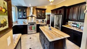 A modern kitchen with dark wood cabinets, stainless steel appliances, and a marble island.