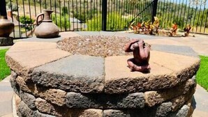 A stone fire pit with a decorative sculpture in the center, surrounded by a stone wall and a metal fence.