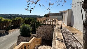 Eine steinerne Treppe mit einer Brüstung führt zu einem Balkon mit Blick auf eine Straße und Grünflächen.