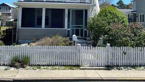 A two-story residential house with a balcony, a front porch, and a picket fence. - Oysterhaven Cottage with partial Water views! New balcony! Close to Fairgrounds! (Chincoteague)