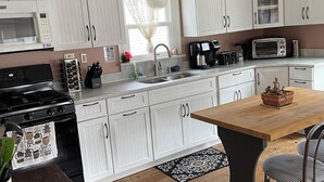A kitchen with white cabinets, a wooden table, and a black stove. - Oysterhaven Cottage with partial Water views! New balcony! Close to Fairgrounds! (Chincoteague)