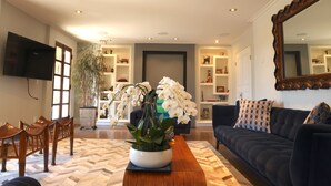 Un salon moderne avec un canapé foncé, des chaises en bois, une table basse et une grande plante en pot.