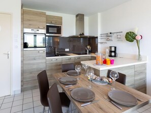 A modern kitchen with built-in appliances, a dining area with a wooden table set for four, and a small island with a coffee maker.