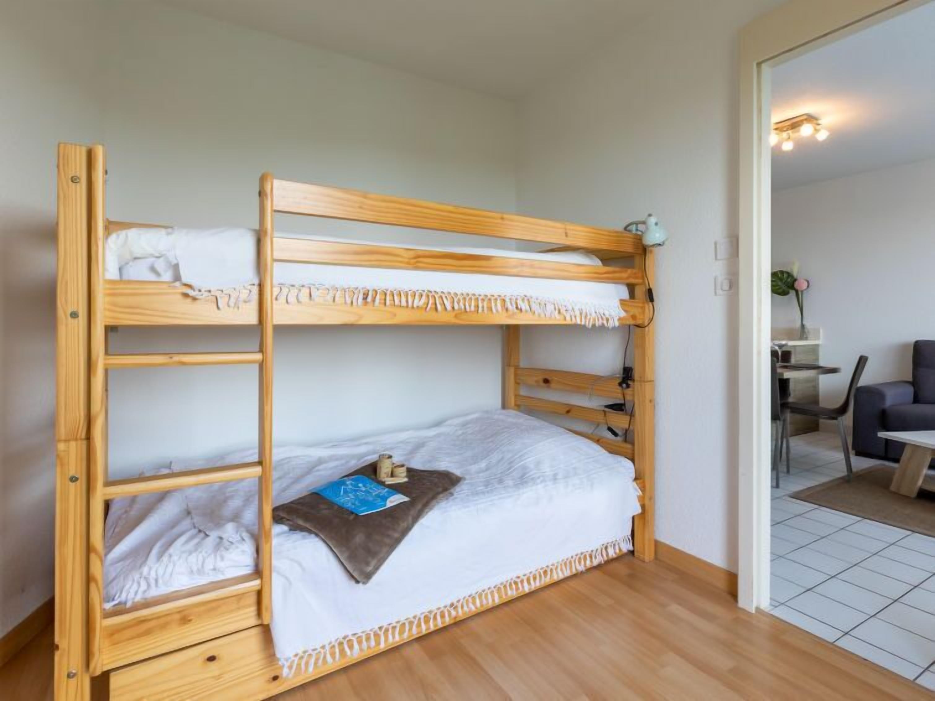 A bunk bed with a wooden frame, a desk, and a chair in the adjacent room.