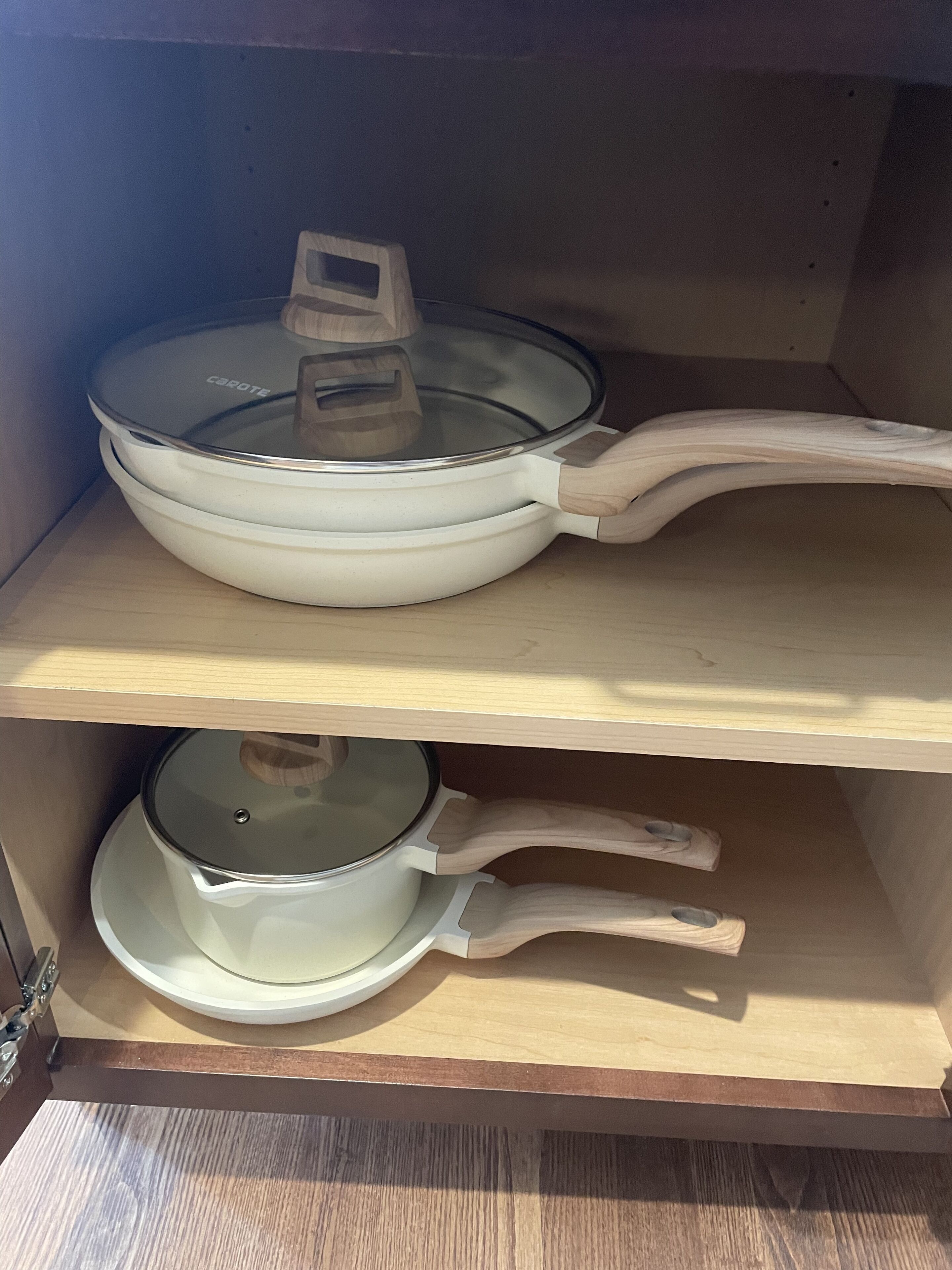 A kitchen cabinet with two white pots, one with a lid and one without.