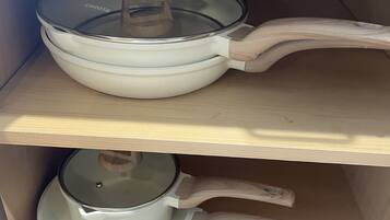 A kitchen cabinet with two white pots, one with a lid and one without.