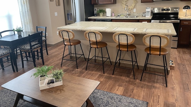A modern kitchen with a central island, bar stools, wooden cabinets, stainless steel appliances, and a dining area with a table and chairs. - PERFECT 2 bedroom, 1 bath Condo (Helena)