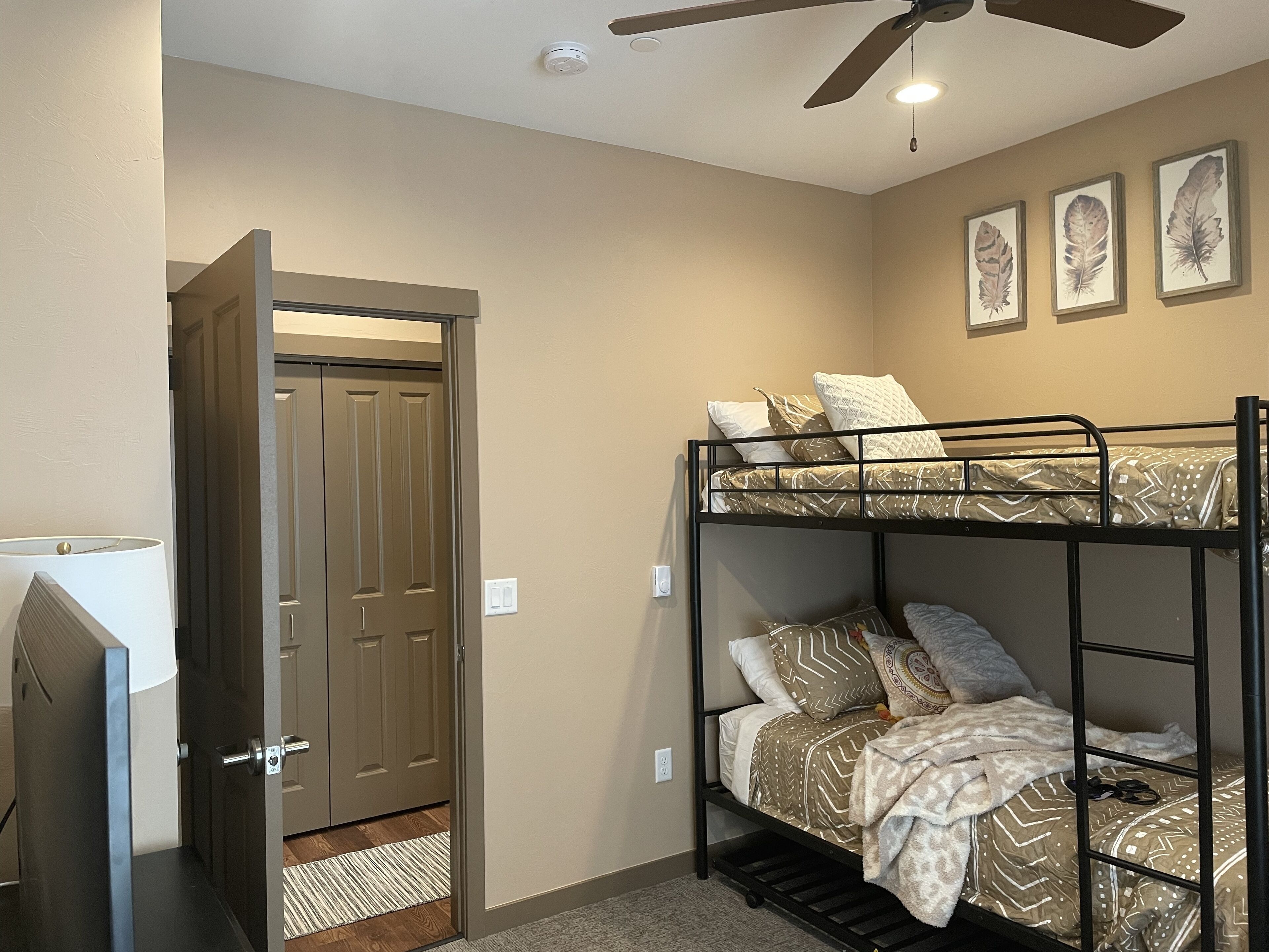 A bunk bed room with a ceiling fan, a door, and three framed leaves on the wall.