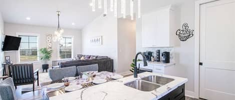 Eine moderne Küche mit Marmorarbeitsplatte, integriertem Spülbecken und einer Essecke mit grauem Sofa und blauen Stühlen.