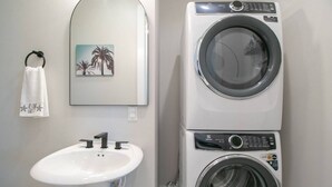 Un baño con lavamanos, un perchero con toalla y lavadora y secadora apiladas.