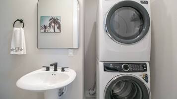 Een badkamer met een wastafel, een handdoekrek met een handdoek, en een gestapelde wasmachine en droger.