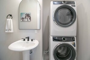 Un baño con lavamanos, un perchero con toalla y lavadora y secadora apiladas.