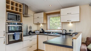 A compact kitchen with built-in appliances, a window with blinds, and a wooden floor. - 1 bedroom accommodation in Mullion Cove, Helston (Mullion Cove, Helston)