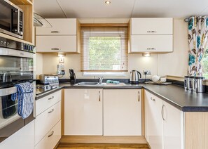 Une cuisine moderne dotée d’appareils électroménagers intégrés, d’une fenêtre avec stores et d’un plancher en bois.