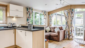 A modern kitchen with wooden cabinets, a black countertop, and a built-in oven. There is a seating area with a brown sofa and a dining table. - 1 bedroom accommodation in Mullion Cove, Helston (Mullion Cove, Helston)