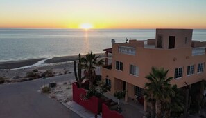 Un edificio moderno con techo plano, varias ventanas y un balcón con vista al mar al atardecer.