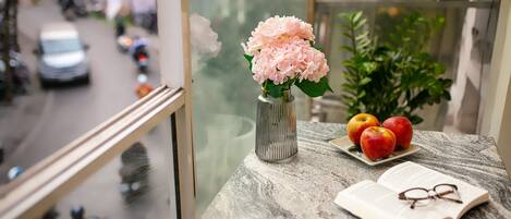 A marble table with a vase of flowers, a plate of apples, and an open book with glasses on it.