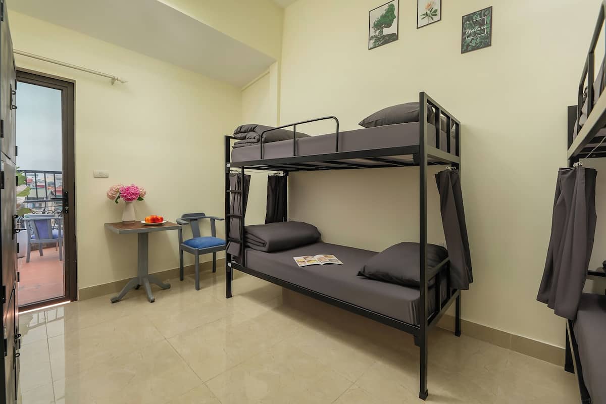 Une chambre avec un lit superposé, une petite table et une chaise, une fenêtre avec des rideaux et une porte donnant sur un espace extérieur.