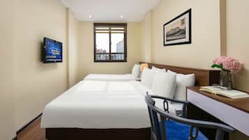 A hotel room with a large bed, a desk with a chair, a television, and a window with a view of buildings.