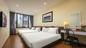 Een hotelkamer met twee bedden, een bureau, een stoel, een raam met gordijnen, een lijst met foto aan de muur en een lamp.