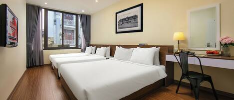 A hotel room with two beds, a desk, a chair, a window with curtains, a framed picture on the wall, and a lamp.