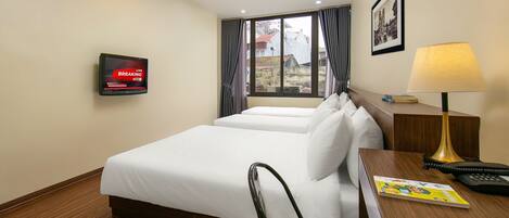 A hotel room with a bed, a desk, a lamp, a TV, and a window with curtains.