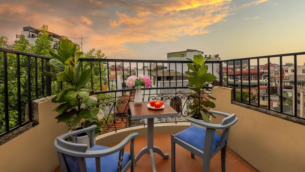 Een balkon met een tafel, twee stoelen, een vaas met bloemen en een schaal fruit.