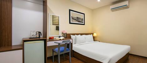 Habitación de hotel con cama, escritorio, silla y un refrigerador pequeño.