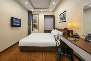 Habitación de hotel con cama, escritorio con lámpara, televisor en la pared y ventana con cortinas.