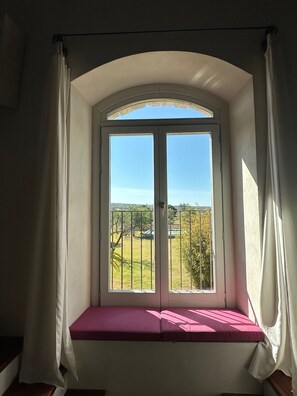 A room with a window seat, white curtains, and a view of a green landscape.