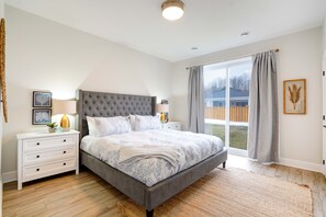 Une chambre avec un grand lit, une table de chevet, une lampe et une fenêtre avec des rideaux.